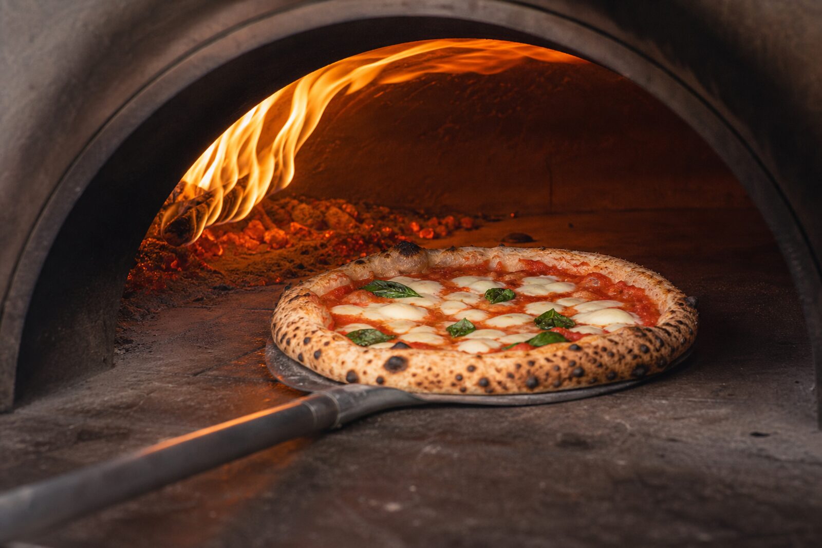 A pizza cooking beside live flame in the van's wood-fired oven